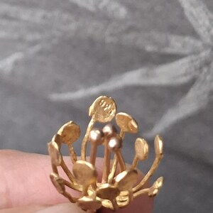 May include: A gold-colored metal jewelry piece shaped like a flower with thin stems topped by small circular discs and three central rounded stamens. One of the outer discs features the stamped text 925, indicating the metal purity of the item.
