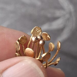 May include: A gold-toned metal jewelry piece shaped like a flower with multiple thin stems topped by small, flat, circular discs. One of the top discs features a clearly visible stamp with the text 925, indicating the metal content of the item.