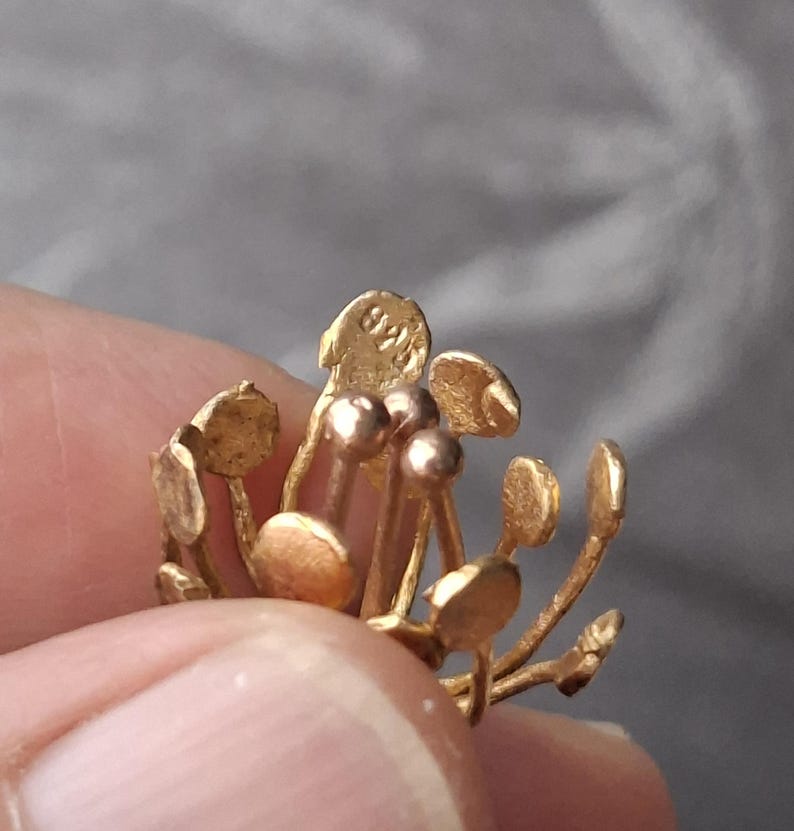 May include: A gold-toned metal jewelry piece shaped like a flower with multiple thin stems topped by small, flat, circular discs. One of the top discs features a clearly visible stamp with the text 925, indicating the metal content of the item.