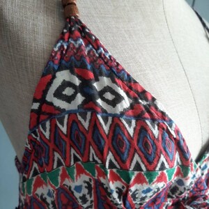 May include: A red, blue, green, and white patterned halter top with a wooden bead accent at the top of the straps.