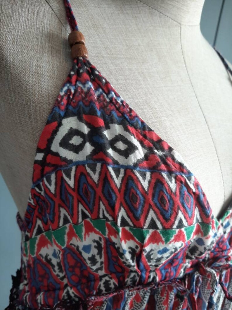 May include: A red, blue, green, and white patterned halter top with a wooden bead accent at the top of the straps.