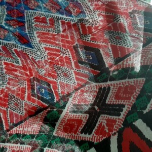 May include: A close-up of a colorful fabric with a geometric pattern. The fabric is red, blue, black, white, and green. The pattern is made up of diamonds and dots.