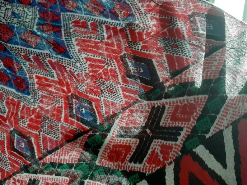 May include: A close-up of a colorful fabric with a geometric pattern. The fabric is red, blue, black, white, and green. The pattern is made up of diamonds and dots.