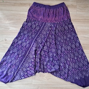 Op de afbeelding: Een paarse rok met een elastische tailleband en een herhalend ruitvormig ikat-patroon in tinten lichtpaars, donkerpaars en wit. Het kledingstuk heeft een uitlopende, asymmetrische zoom en een vloeiend, ruimvallend silhouet.
