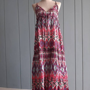 May include: A long, sleeveless maxi dress with a geometric pattern in shades of red, blue, and black. The dress has a V-neckline and a tiered skirt.