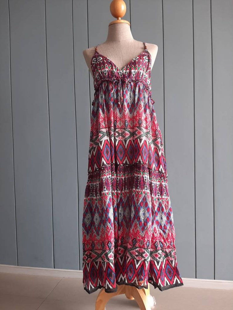 May include: A long, sleeveless maxi dress with a geometric pattern in shades of red, blue, and black. The dress has a V-neckline and a tiered skirt.