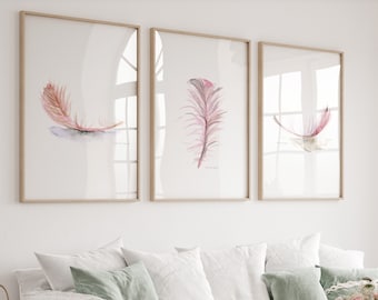 Puede incluir: Tres pinturas de acuarela enmarcadas de plumas rosas en una pared blanca sobre un sofá blanco con almohadas verdes y blancas. Un ramo de flores rosas en un jarrón de vidrio se encuentra sobre una mesa de café de madera.