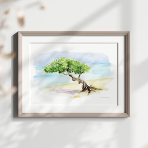 May include: Watercolour painting of a tree on a beach with blue water and a light blue sky. The tree is green and has a thick trunk. The painting is framed in a light brown frame.