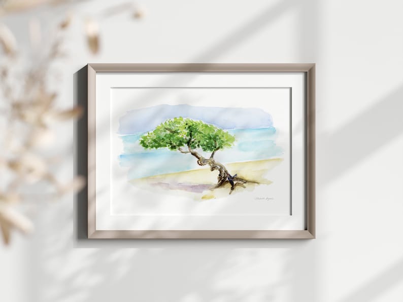 May include: Watercolour painting of a tree on a beach with blue water and a light blue sky. The tree is green and has a thick trunk. The painting is framed in a light brown frame.