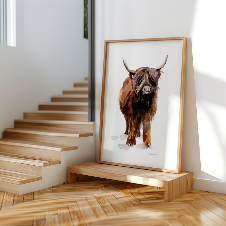 Op de afbeelding: Een aquarel van een bruine Schotse hooglander met lange hoorns en een ruig vacht. De koe staat op een witte achtergrond met een paar lichtbruine voetafdrukken.