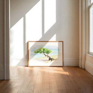 May include: A framed watercolour painting of a tree growing on a beach. The tree is green and has a long, twisted trunk. The beach is white and the water is blue. The painting is in a light wood frame.