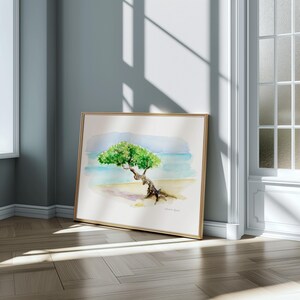 May include: A watercolour painting of a solitary tree on a beach. The tree is green and has a thick trunk. The beach is sandy and the water is blue. The painting is framed in a gold frame.