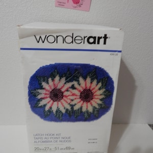 May include: A Wonderart latch hook kit featuring a design of two sunflowers with red and white petals on a blue background. The box is labeled with the text "LATCH HOOK KIT" and measurements of 20 x 27 inches.