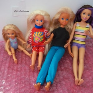 May include: Four dolls, three with long blonde hair and one with purple hair, are sitting on a pink bubble wrap surface. The dolls are wearing different outfits, including a red and white striped shirt with a yellow and blue design, a black shirt with blue pants, a striped tank top with purple shorts, and a blue swimsuit.