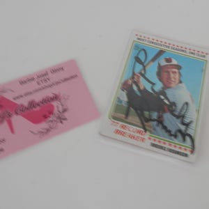May include: A pink business card with the text "The Collection" and a red shoe graphic. A baseball card with a photo of a baseball player in a white uniform with the text "Record Breaker" and "Brooks Robinson" on the card.