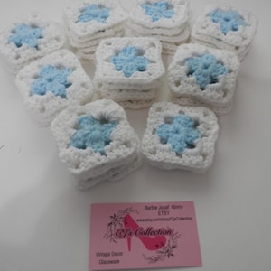 May include: A collection of white crocheted squares with blue flower accents. The squares are stacked on top of each other. The image also includes a business card with the text "Barbie Joset Ginny ETSY www.etsy.com/shop/CJzCollection CJzCollection Vintage Decor Glassware".