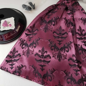 May include: A pink and black patterned fabric skirt with a satin finish. The fabric has a damask design. The skirt is part of a Barbie Holiday Traditions doll outfit.
