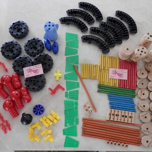 May include: A collection of colorful toy building blocks and components, including black wheels, curved black pieces, green panels, red connectors, and wooden dowels. Various shapes and sizes are present, suggesting a construction toy set.