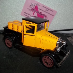 May include: A yellow and black toy pickup truck with a black roof and a bed full of orange barrels. The truck has a brown steering wheel and brown wheels.
