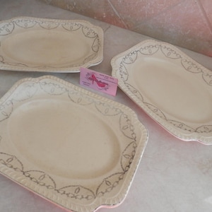 May include: Three off-white serving platters with decorative silver trim. The platters are rectangular and oval-shaped, with scalloped edges. The platters are arranged on a light-colored surface.