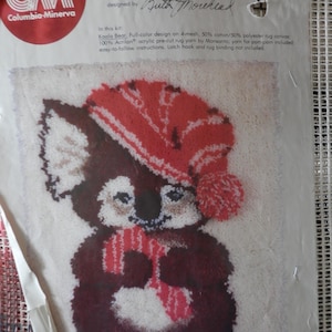May include: A Latch-a-Christmas Rug Kit by Columbia-Minerva. The kit features a Koala Bear design wearing a red and white striped hat and scarf. The rug measures 20" x 24" and includes yarn for the pom-pom. The kit is designed by Ruth Morehead.