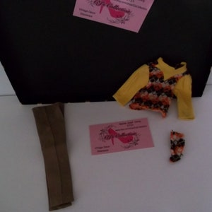 May include: A set of doll clothes including a brown pair of pants, a yellow and orange patterned sweater, and a pair of orange and white patterned tights.