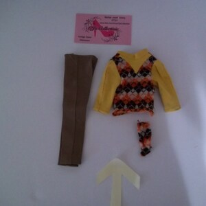 May include: A doll outfit set with a brown pair of pants, a yellow and brown patterned sweater, and a pair of brown and orange socks.