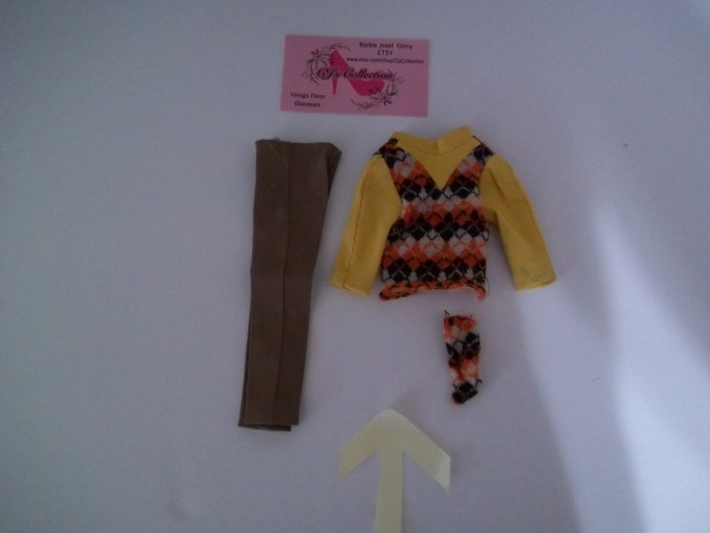 May include: A doll outfit set with a brown pair of pants, a yellow and brown patterned sweater, and a pair of brown and orange socks.