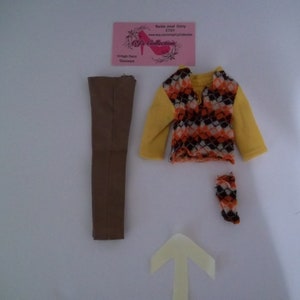 May include: A set of doll clothes including a brown pair of pants, a yellow sweater with a brown, orange, and white geometric pattern, and a pair of orange and brown patterned stockings.