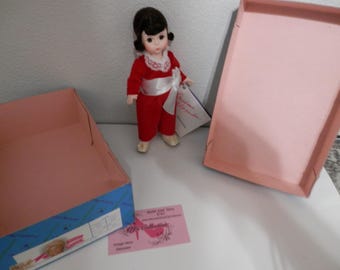 Könnte beinhalten: Eine rot-weiße Puppe, die ein rotes Kleid mit einer weißen Schärpe und weißen Schuhen trägt. Die Puppe sitzt auf einer rosa Box mit einem blau-weißen Muster. Die Box trägt den Text "Vintage Chic Treasures". Es gibt eine weiße Karte mit dem Text "Bride and Groom Collection" darauf.