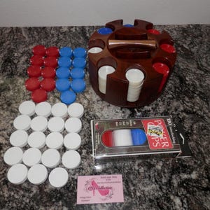 May include: A wooden poker chip holder with a handle, filled with stacks of white chips and surrounded by red, white, and blue poker chips. A box of 100 interlocking poker chips is also present.