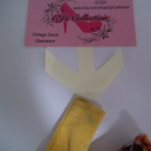 May include: A yellow fabric arrow with a white fabric arrow behind it. The white arrow is pointing down. The text on the pink card reads "Etsy, www.etsy.com/shop/CjsCollection, Cj's Collection, Vintage Decor, Glassware".