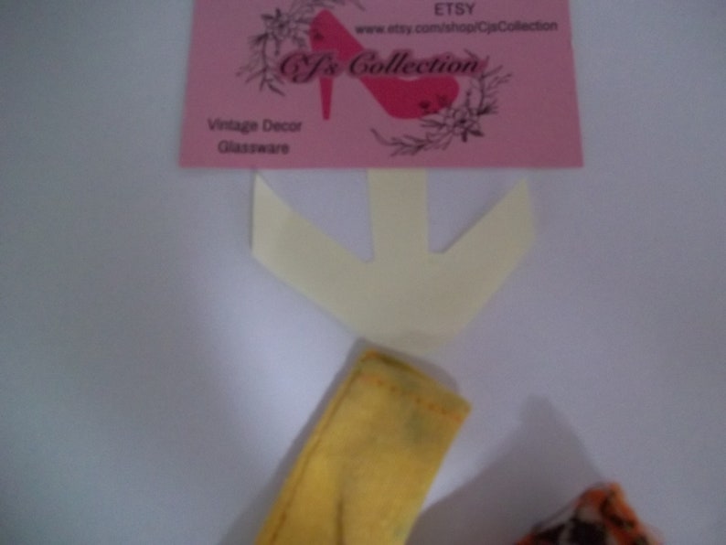 May include: A yellow fabric arrow with a white fabric arrow behind it. The white arrow is pointing down. The text on the pink card reads "Etsy, www.etsy.com/shop/CjsCollection, Cj's Collection, Vintage Decor, Glassware".