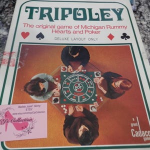May include: A vintage Tripoley board game box. The box features the game's title in green, with the words "The original game of Michigan Rummy Hearts and Poker" below. The image on the box shows four people playing the game. A pink business card is in the lower left corner.