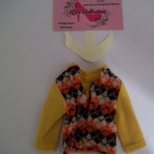 May include: A yellow long-sleeved shirt with a brown, orange, and white patterned vest. The vest has a diamond pattern.
