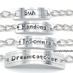May include: Four silver chain bracelets with silver rectangular tags. The tags have the words "Sua", "Handong", "Insomnia", and "Dreamcatcher" engraved on them.