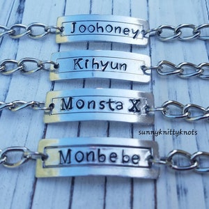 May include: Four silver chain bracelets with rectangular silver tags. The tags are engraved with the names "Joohoney", "Kihyun", "Monsta X", and "Monbebe".
