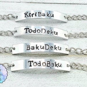 Puede incluir: Cuatro pulseras de cadena plateadas con dijes rectangulares plateados. Cada dije tiene una frase diferente grabada: "Kirri Baku", "TodoDeku", "BakuDeku" y "TodoBaku".