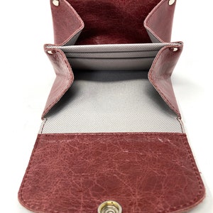 May include: A burgundy leather wallet with a snap closure and multiple compartments. The wallet is open to reveal a gray fabric lining.