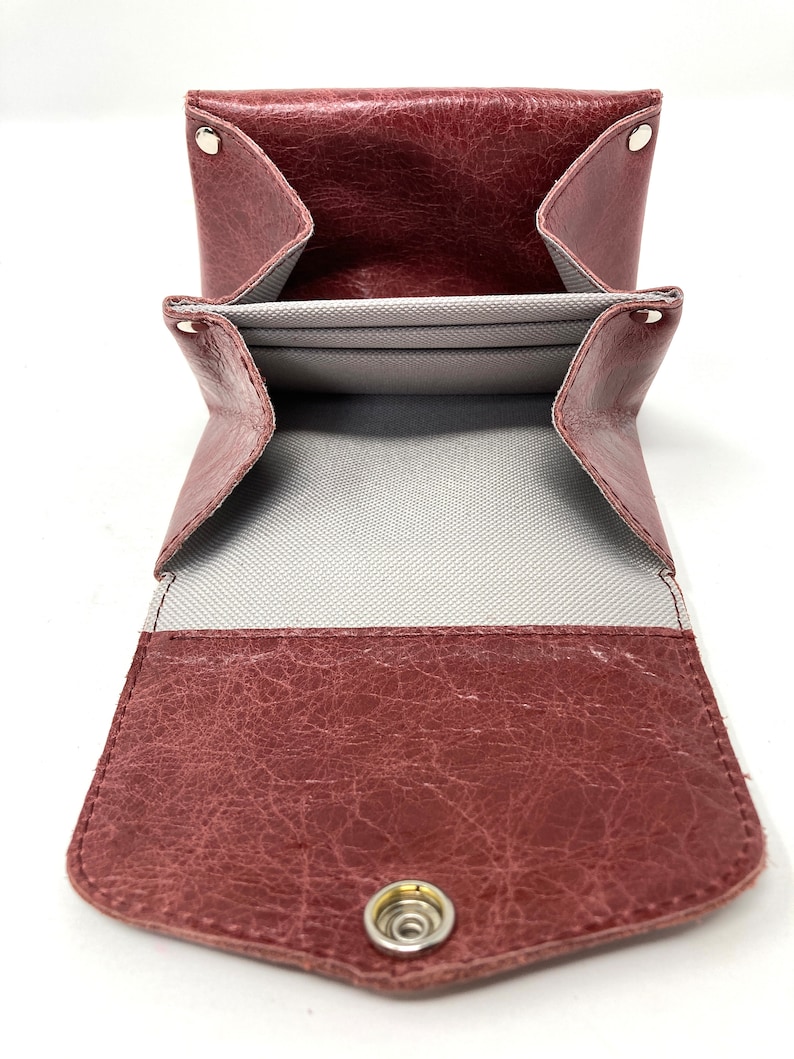 May include: A burgundy leather wallet with a snap closure and multiple compartments. The wallet is open to reveal a gray fabric lining.