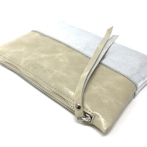 Puede incluir: Un clutch de cuero beige y plateado con cierre de cremallera y una correa larga.