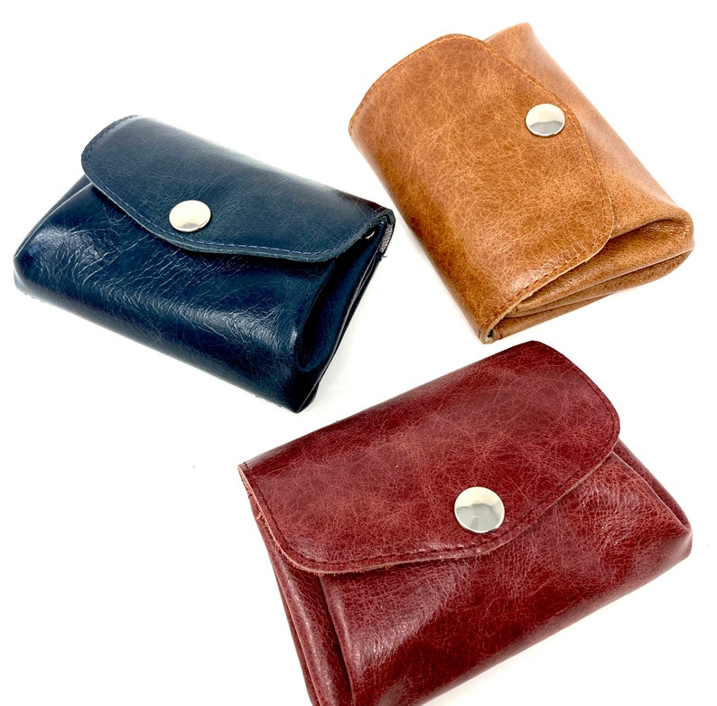 May include: Three leather wallets in different colors: dark blue, brown, and burgundy. Each wallet has a single snap closure and a simple design.