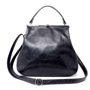 Könnte beinhalten: Eine schwarze Ledertasche mit einem silbernen Verschluss und einem langen, verstellbaren Trageriemen.