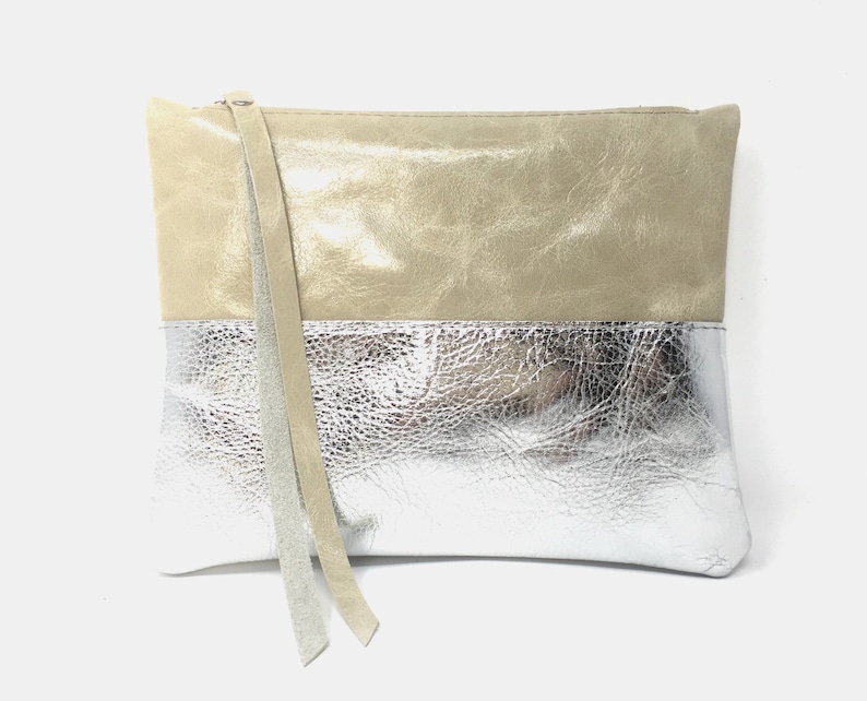 Puede incluir: Un bolso de mano con un dise&ntilde;o de dos tonos. La mitad superior es de cuero beige claro y la mitad inferior es de cuero met&aacute;lico plateado. El bolso tiene una correa larga y fina.