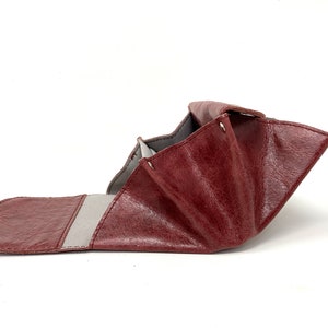 May include: A burgundy leather wallet with a gray fabric interior. The wallet is folded open, revealing the interior.