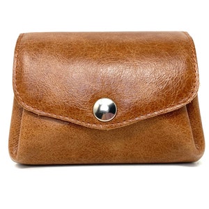 May include: A brown leather coin purse with a snap closure. The purse has a textured surface and a silver button.