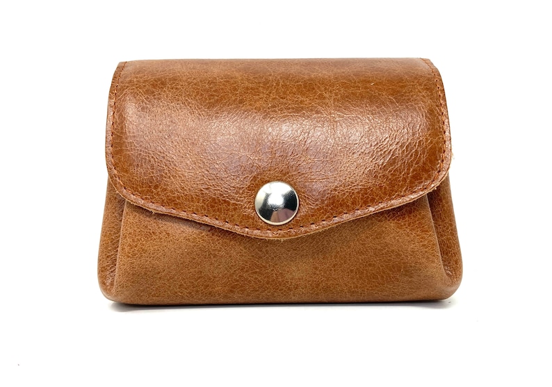 May include: A brown leather coin purse with a snap closure. The purse has a textured surface and a silver button.