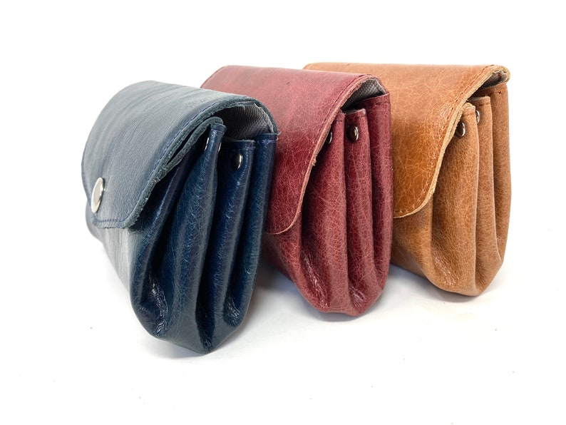 May include: Three leather wallets in different colors: navy blue, burgundy, and brown. The wallets are folded and have a flap closure.