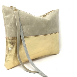 Puede incluir: Un peque&ntilde;o bolso de mano rectangular hecho de cuero. La mitad superior del bolso es de color gris claro y la mitad inferior es de color dorado. El bolso tiene una cremallera y una correa larga y fina.