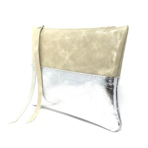 Puede incluir: Un clutch de cuero beige y plateado con una correa larga beige. El clutch tiene una cremallera.